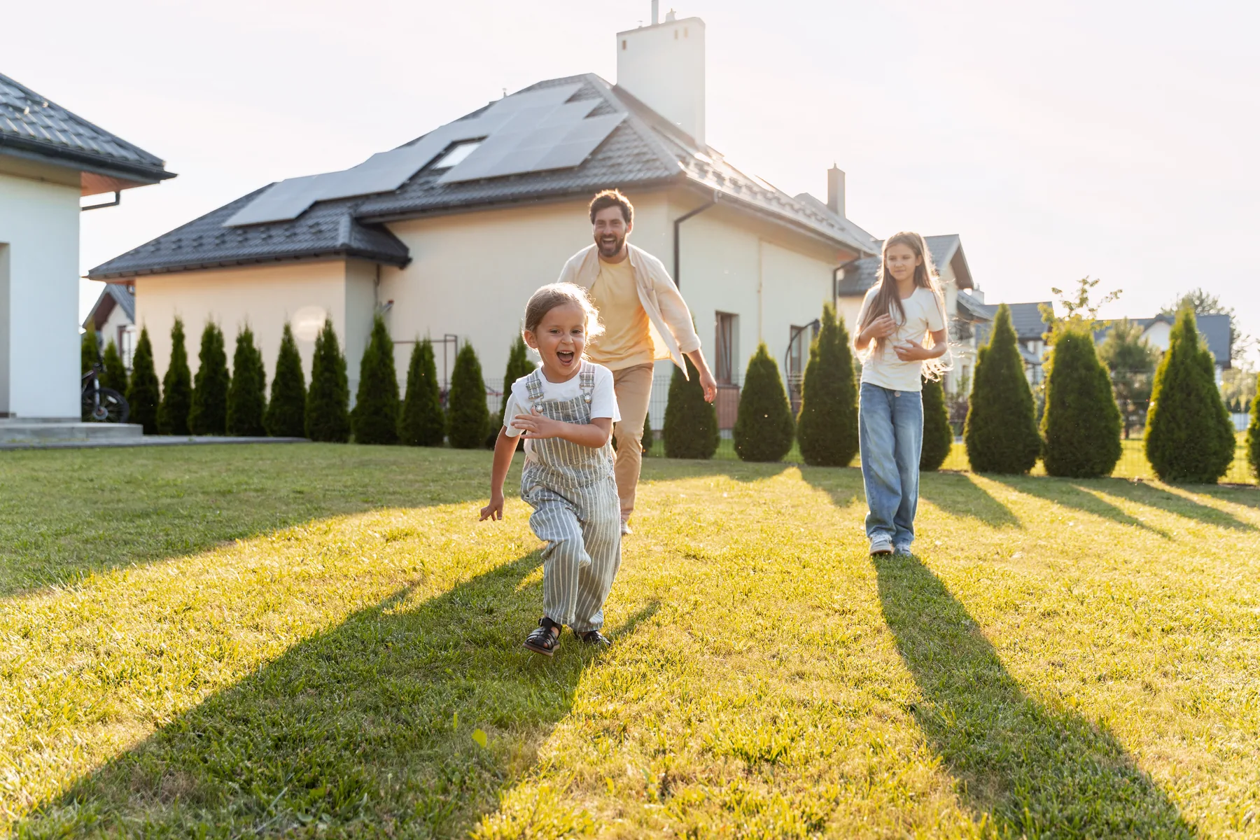 Famille devant maison équipée de panneaux photovoltaïques au coucher de soleil